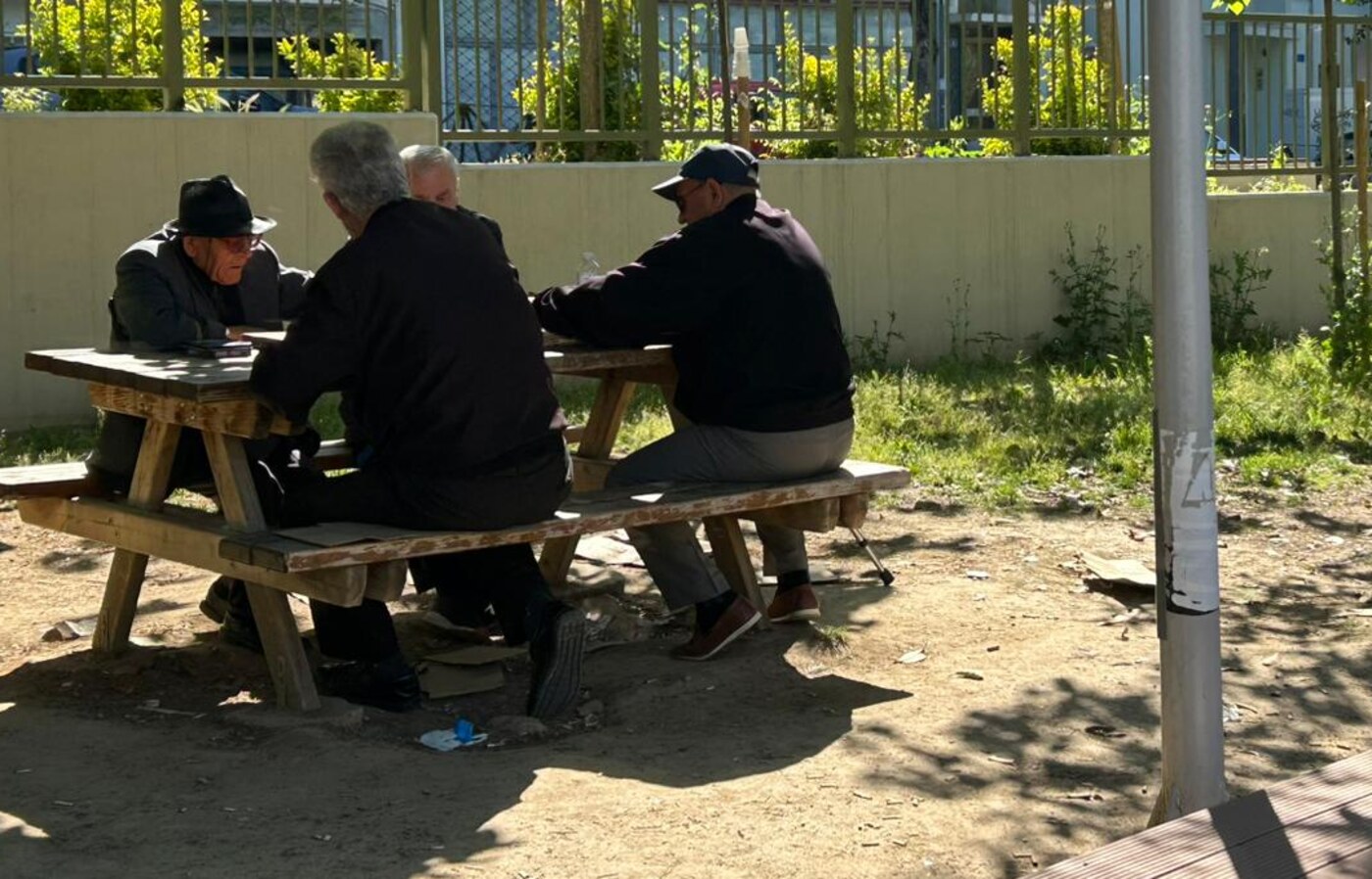 Patru bărbați vârstnici jucând cărți la o masă de lemn, la umbră
