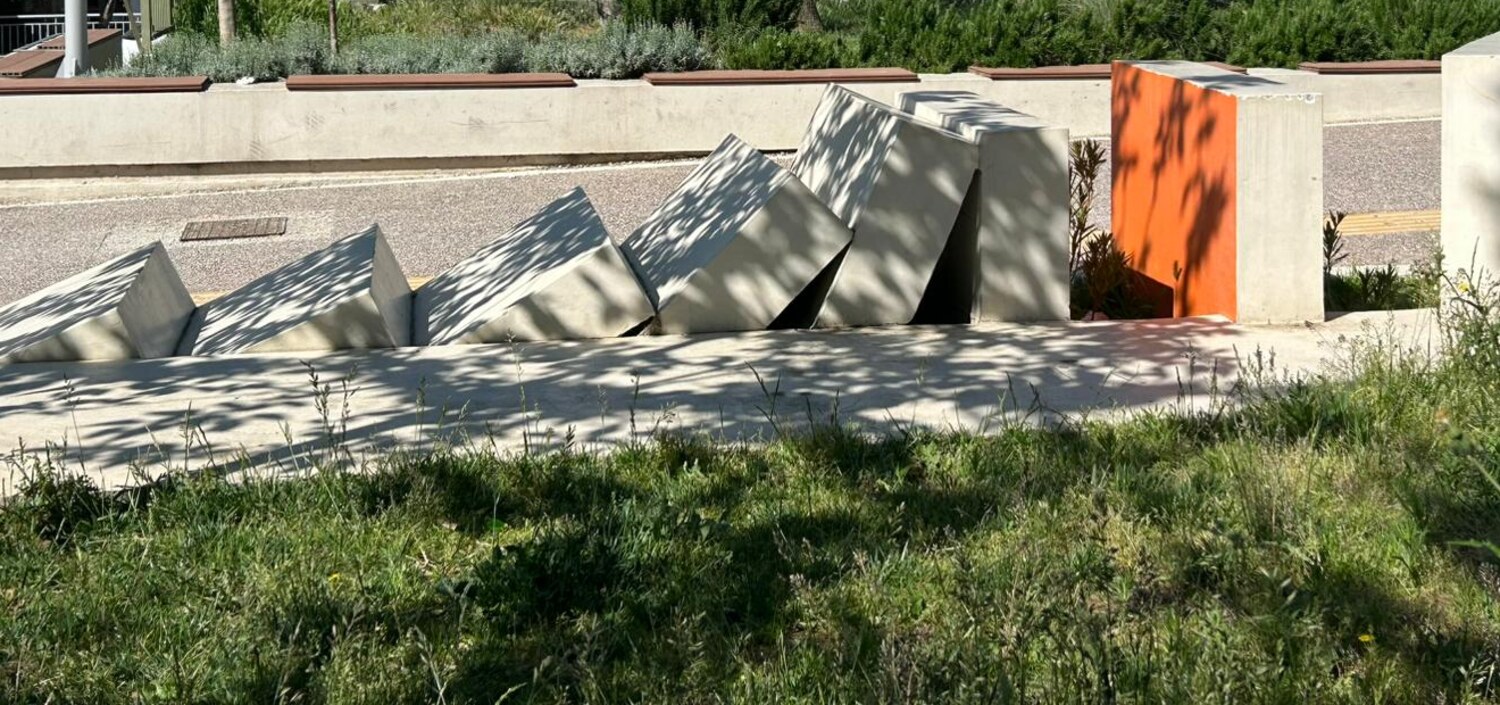 Șir de lespezi de beton înclinate, în iarbă, lângă aleea parcului
