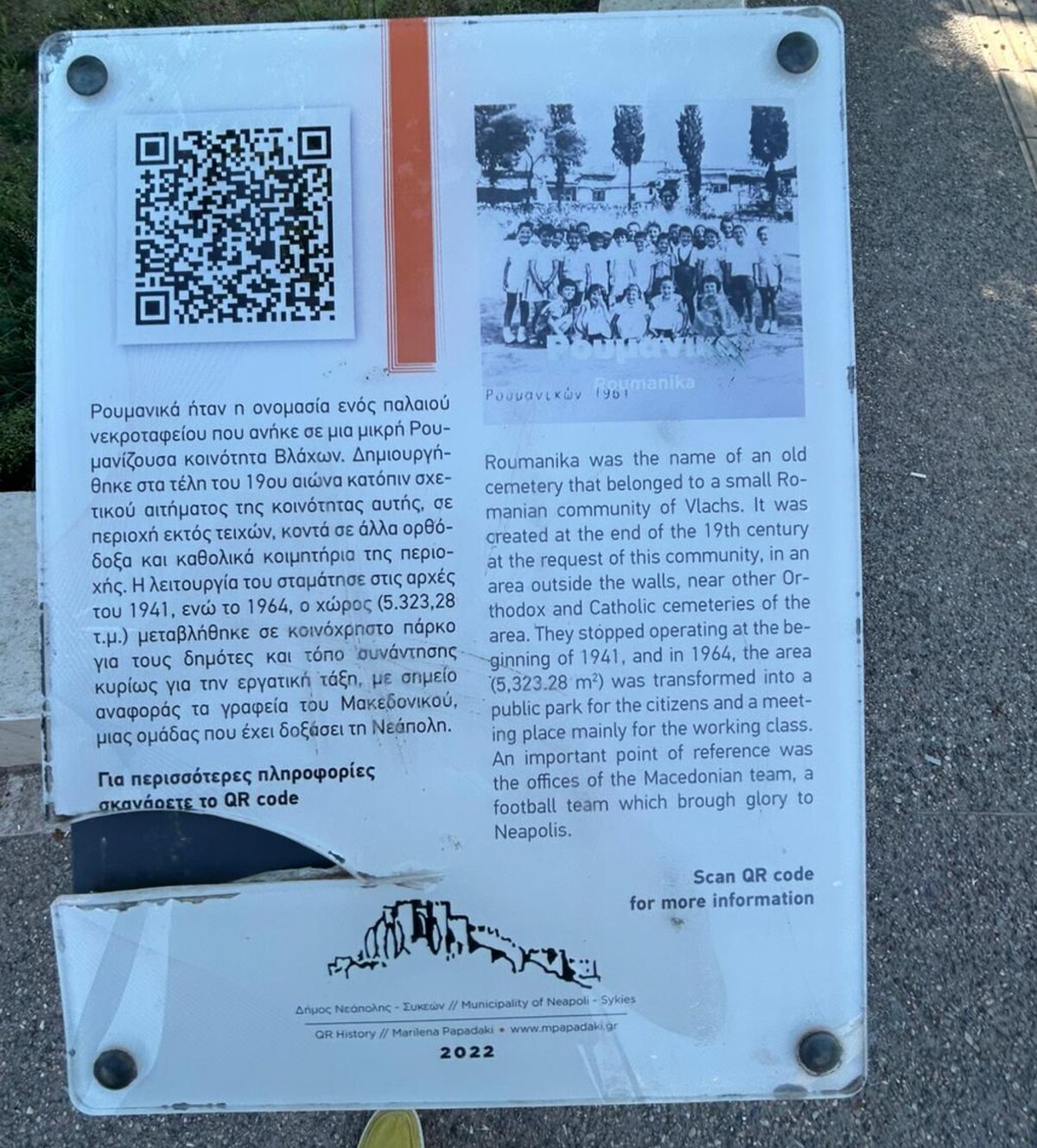 Panou informativ bilingv, cu o fotografie veche de grup și text în greacă și engleză